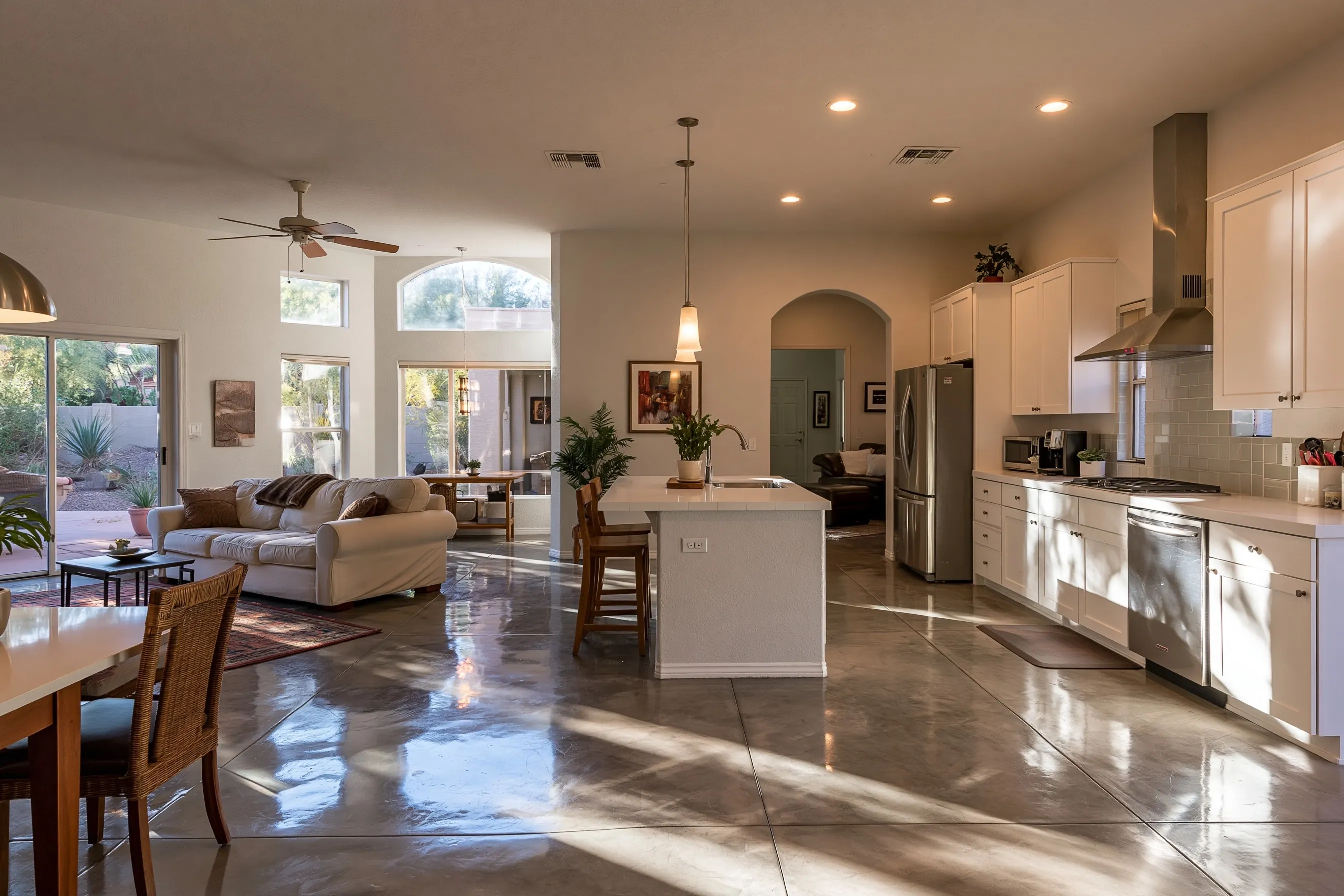 Kitchen and great room of a newer Phoenix-valley house with a warm grey polished concrete floor, white shaker cabinets and window light reflecting on the floor